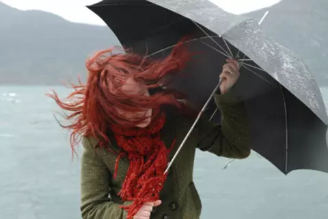 Junge Frau kämpft mit einem Schirm gegen den Wind an