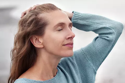 Frau mit geschlossenen Augen fährt sich mit einer Hand durch die Haare