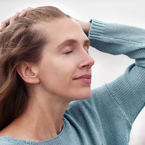 Frau mit geschlossenen Augen fährt sich mit einer Hand durch die Haare